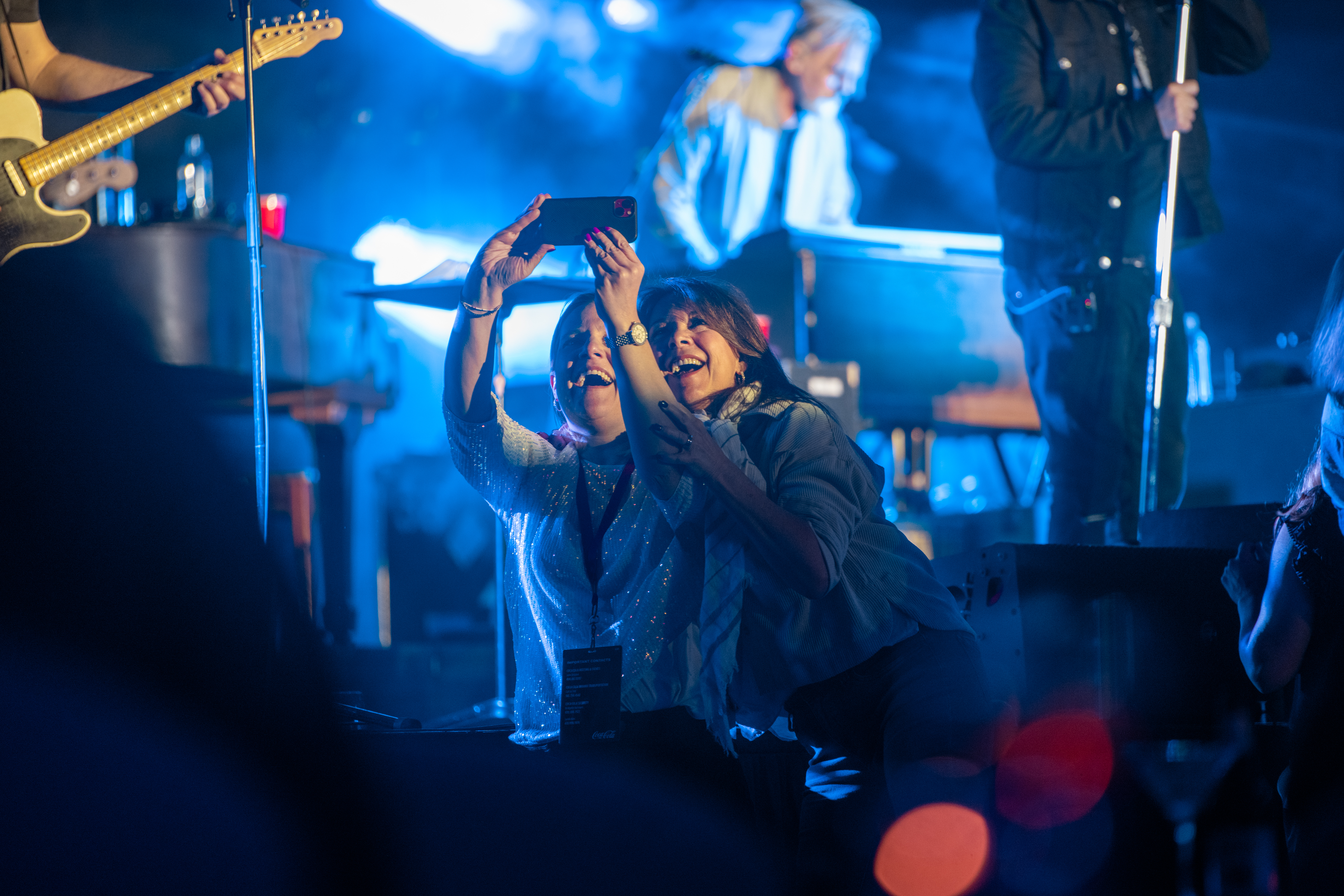 Two women taking selfie at Coca-Cola's private concert during 2024 Final Four in Scottsdale hangar.
