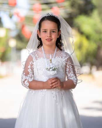 Portrait of a young girl holding a rosary in her white lace First Holy Communion dress and veil.