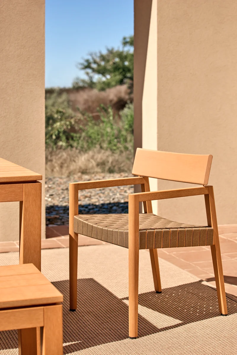 Kubik outdoor dining chair with warm TechTeak frame and woven seat beside a dining table.