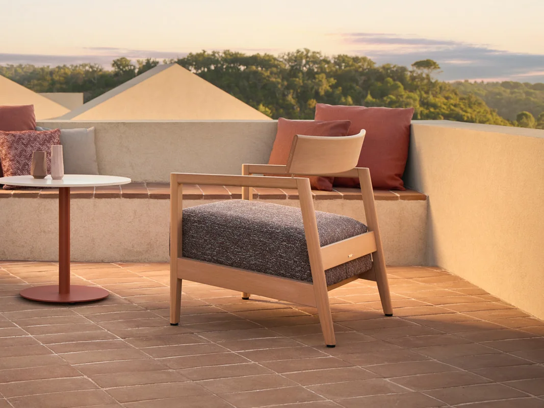 Kubik outdoor lounge chair with soft upholstery and warm TechTeak frame on an architectural terrace.