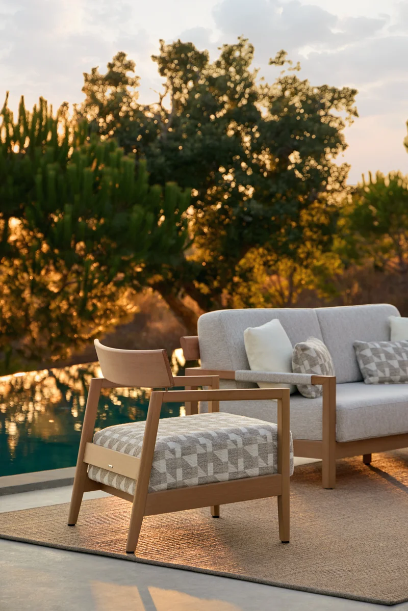 Kubik lounge armchair and outdoor sofa beside a pool, showing refined cushions and warm TechTeak detailing.