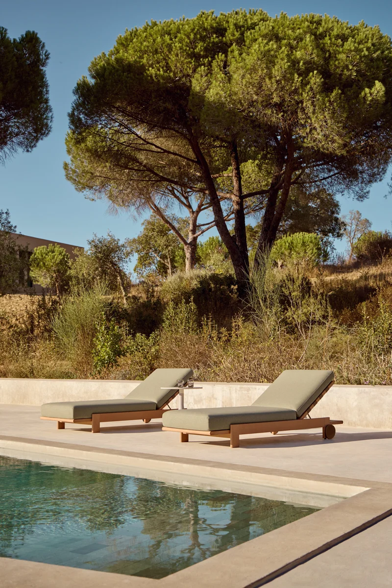 POINT Rivoli lounger beside a swimming pool with timber frame, soft green cushion and patterned outdoor head cushion.