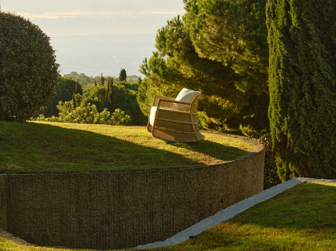 Wide shot of the ESCALA Rocking Chair in natural linen on a garden lawn