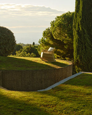 Wide shot of the ESCALA Rocking Chair in natural linen on a garden lawn