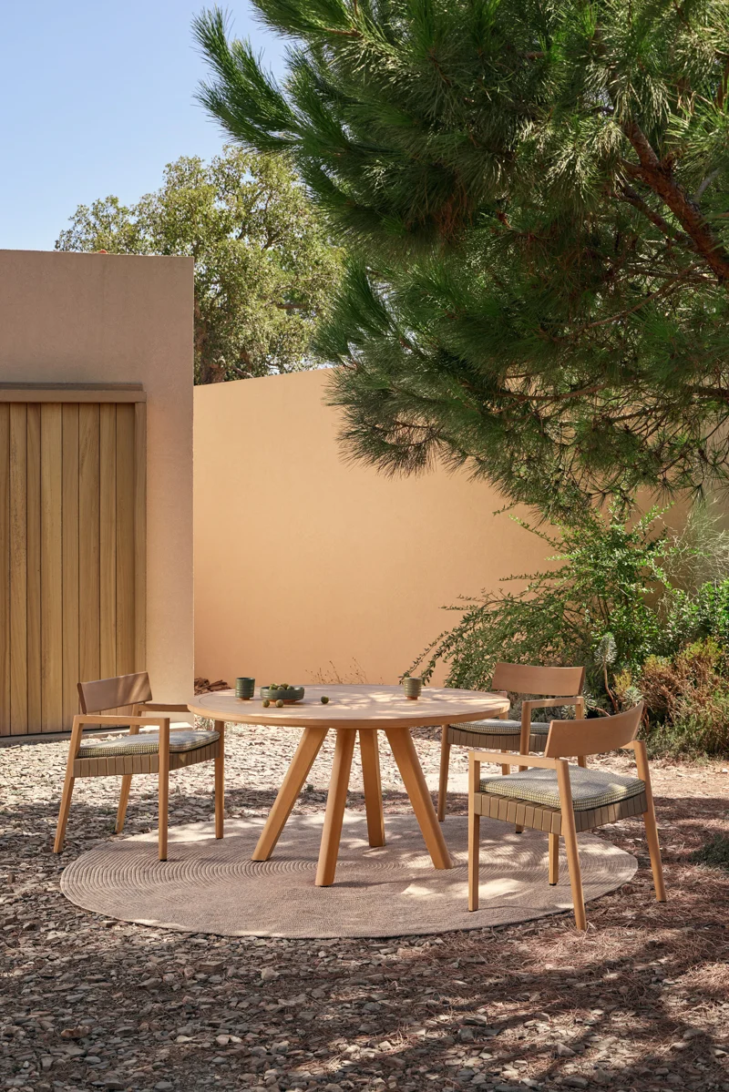 Round Kubik outdoor dining table with chairs, set beneath trees in a refined courtyard setting.