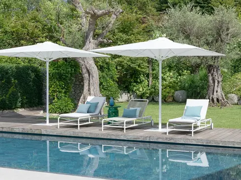 Poolside arrangement of AIR Sun Loungers under umbrellas in a lush garden setting