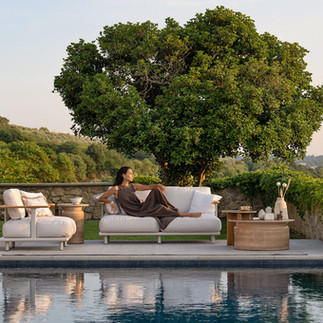 Atmosphera Bliss outdoor sofa with cream cushions and low table beside a pool, framed by trees and landscape planting.