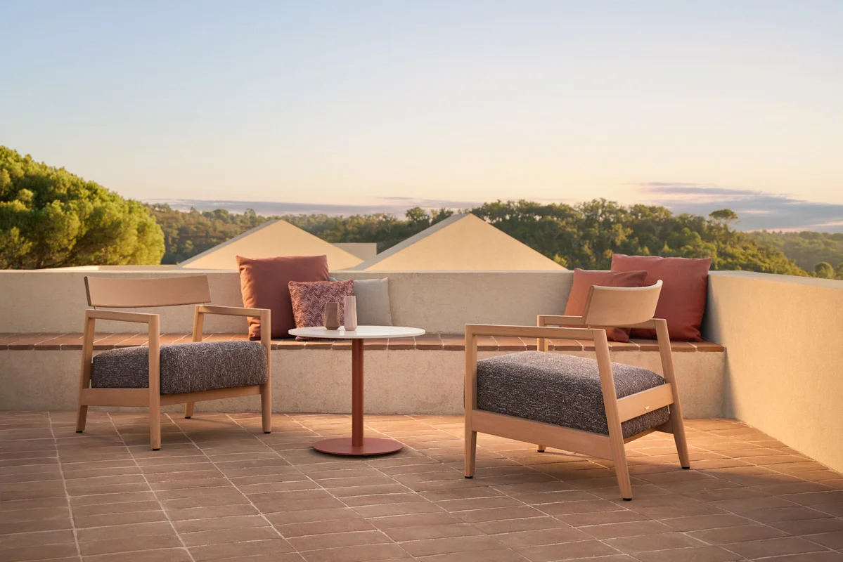 Kubik outdoor lounge chairs on a terrace with soft upholstery, warm frame tones and low architectural tables.