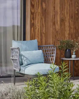 CURIO Armchair positioned on a stylish outdoor patio with lush greenery.