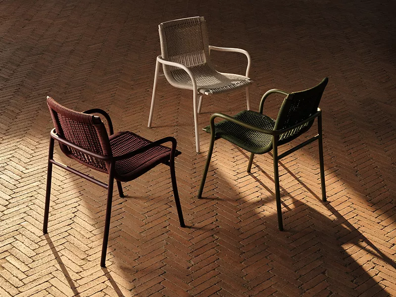 Three Ethimo outdoor chairs in deep red, cream and green woven finishes on warm brick flooring.