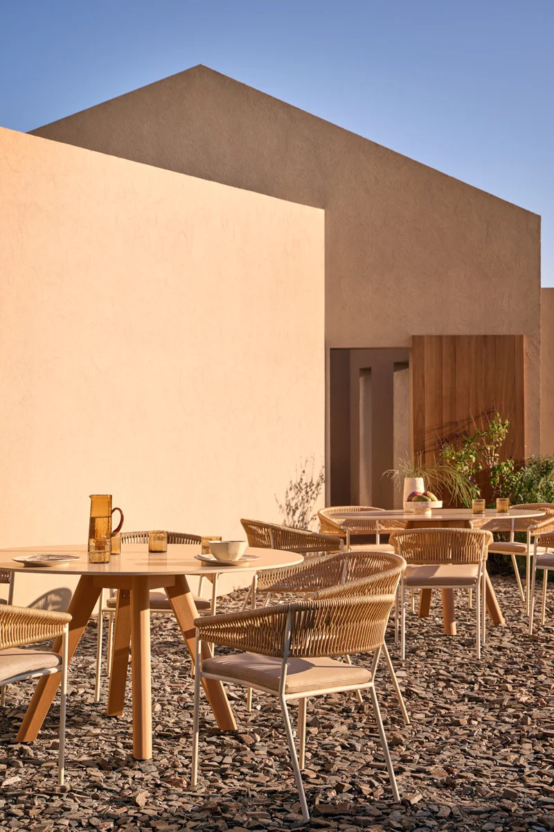 Kubik outdoor dining chairs and round tables arranged beside a warm architectural exterior.
