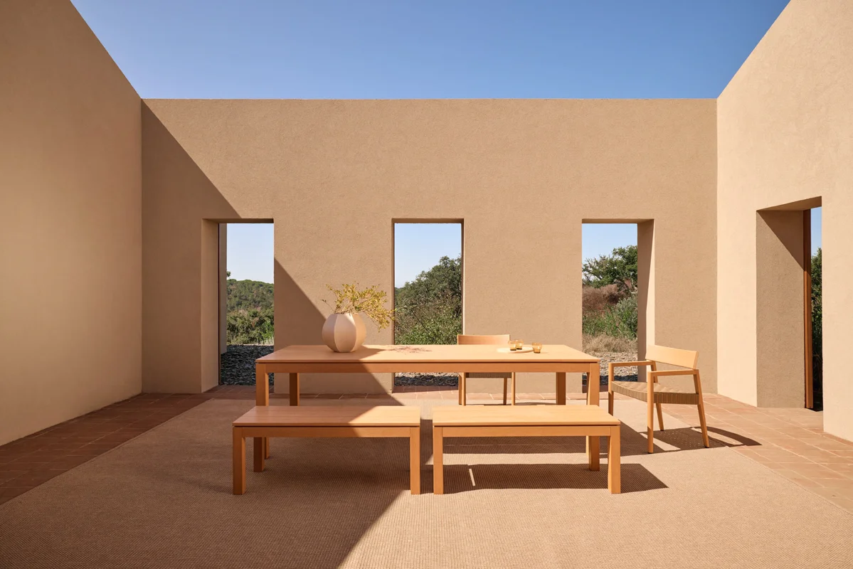 Kubik outdoor dining table and benches arranged in a sheltered architectural outdoor dining space.