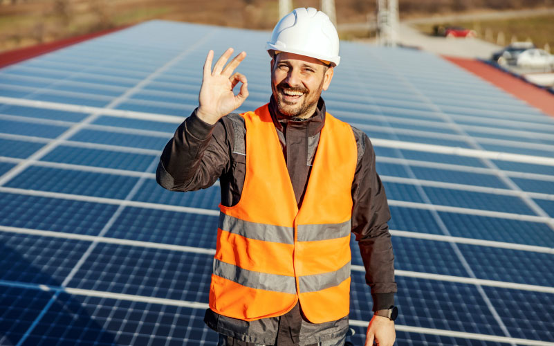 Mann vor PV-Modulen in Warnweste.