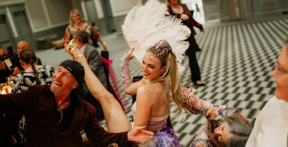 Burlesque dancer at wedding event posing with guests laughing