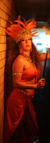 Fire dancers dressed in orange tribal Aztec themed costume holding a fire prop