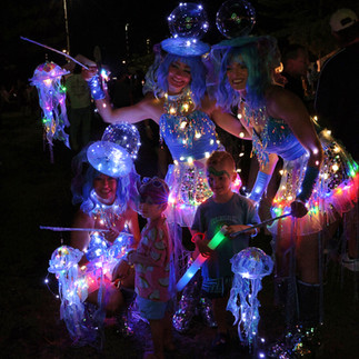 three roving performers dressed in glowing lED jellyfish costumes posing at festival with children for photographs in the Central coast