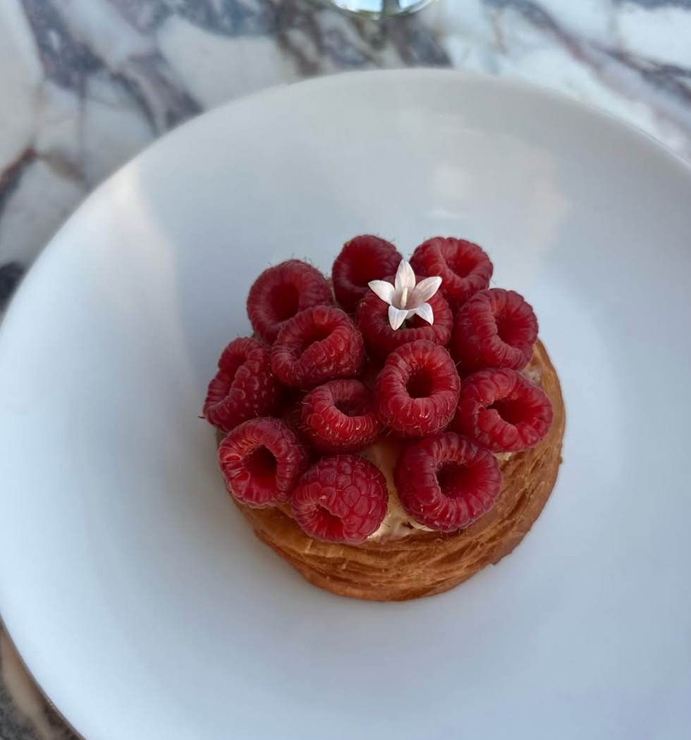 Pastry topped with fresh raspberries and a white flower on a white plate. Background is a marble surface. Vibrant and appetizing.
