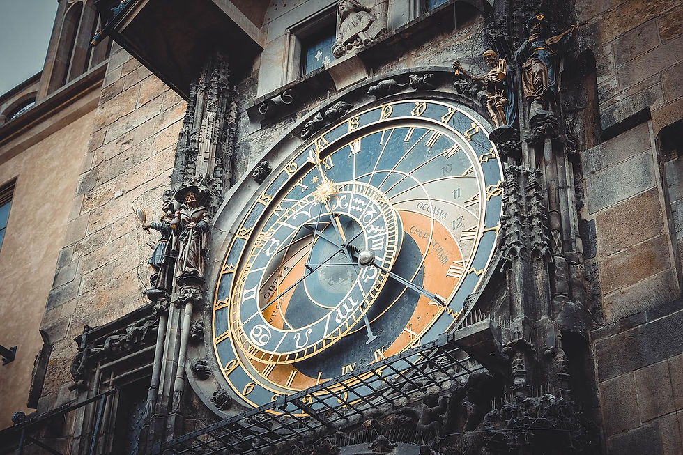 Ornate astronomical clock on a stone building, featuring Roman numerals and gold details. Sculptures frame the colorful, intricate face.