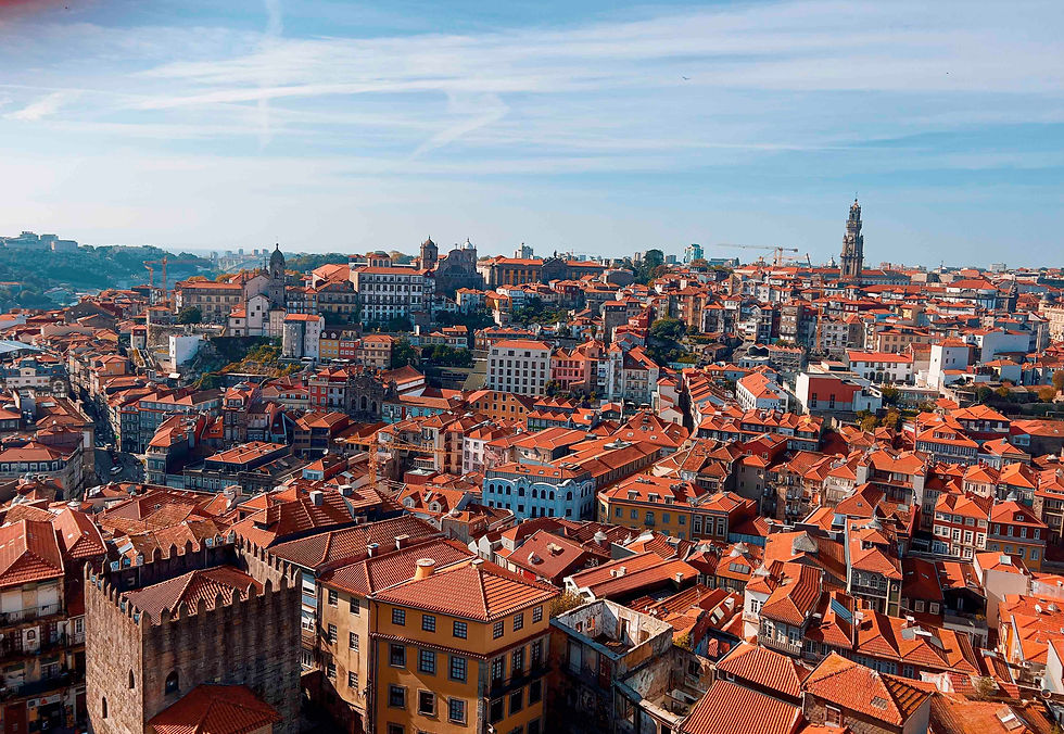 Aerial view of a European city with red-tiled roofs, historic buildings, and clear blue sky. Urban landscape with vibrant colors.