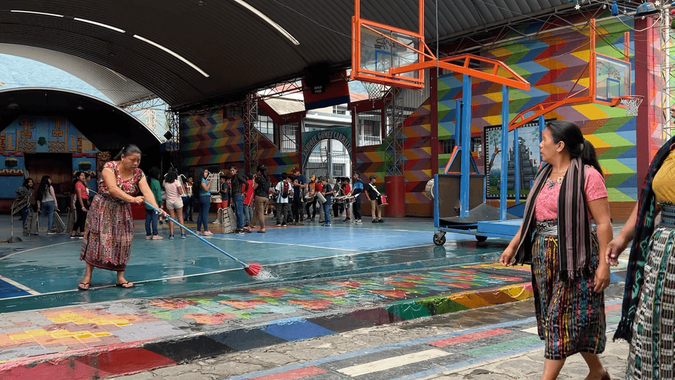 San Juan colorful open-air gymnasium passing a group of kids practicing for the marching band, as women in traditional huipiles pass by.
