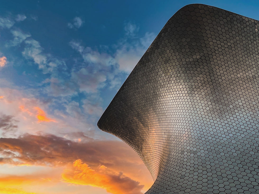 Modern building with hexagonal pattern and curved design, set against a sunset sky with vibrant orange clouds and a blue backdrop.