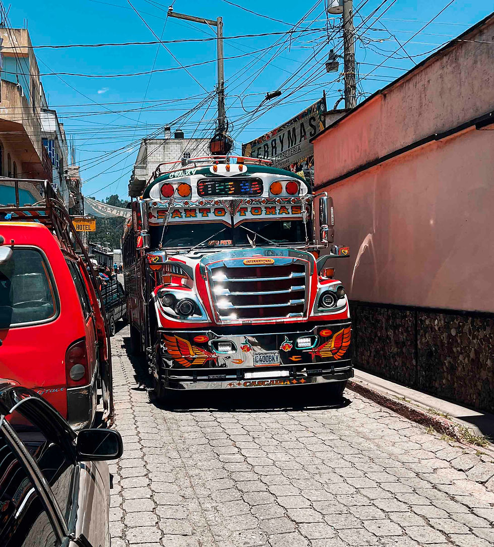 Colorful bus labeled "Santo Tomas" on a narrow, cobblestone street between buildings. Visible wires overhead under a clear blue sky.