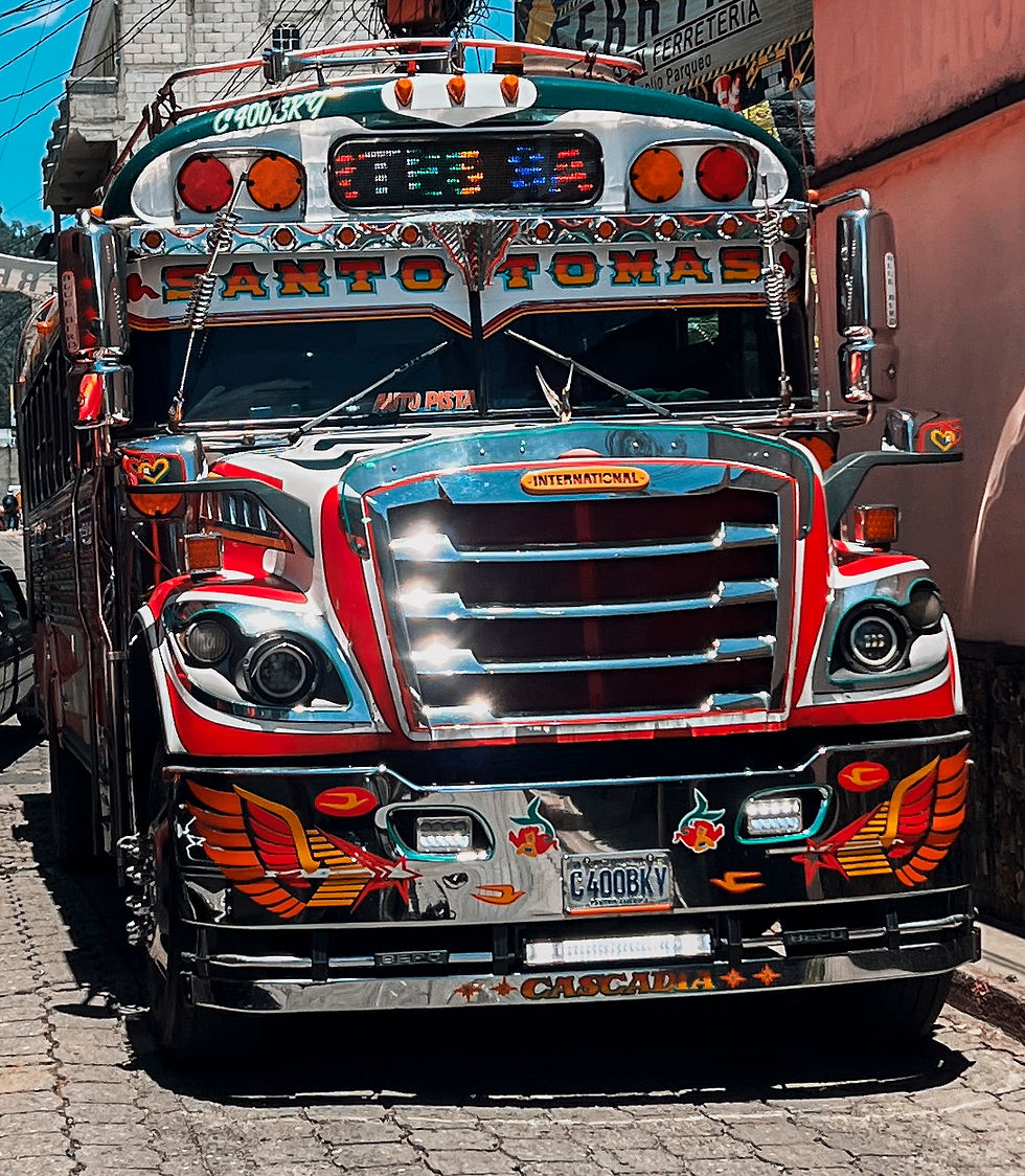 Colorful decorated chicken bus labeled "Santo Tomas" parked on a cobblestone street. Bright chrome and vibrant patterns, sunny day ambiance.