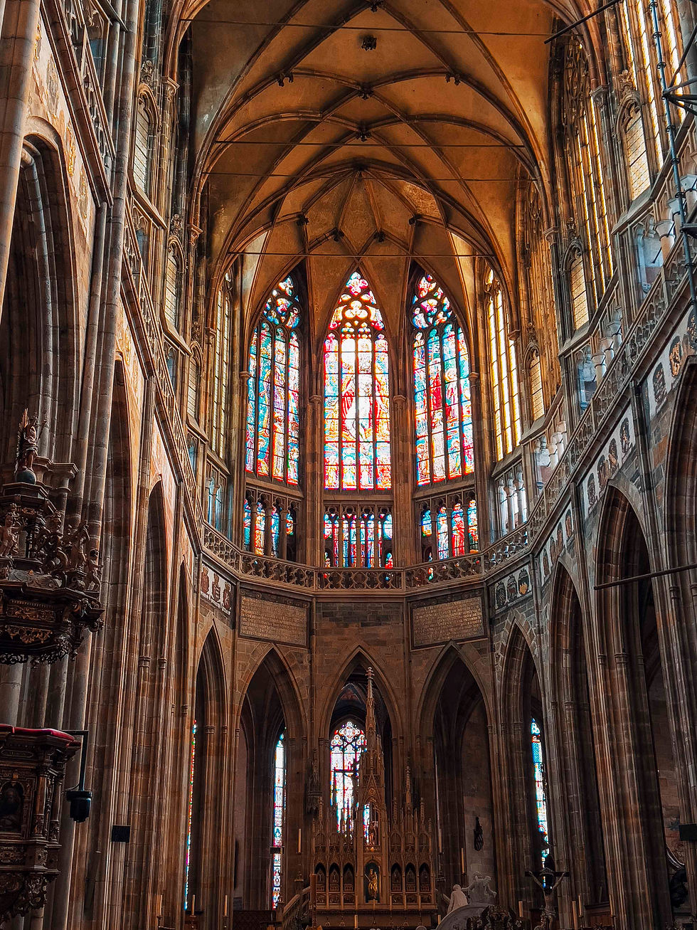 Gothic cathedral interior with towering stained glass windows casting colorful light on stone arches. Ornate altar is visible below.