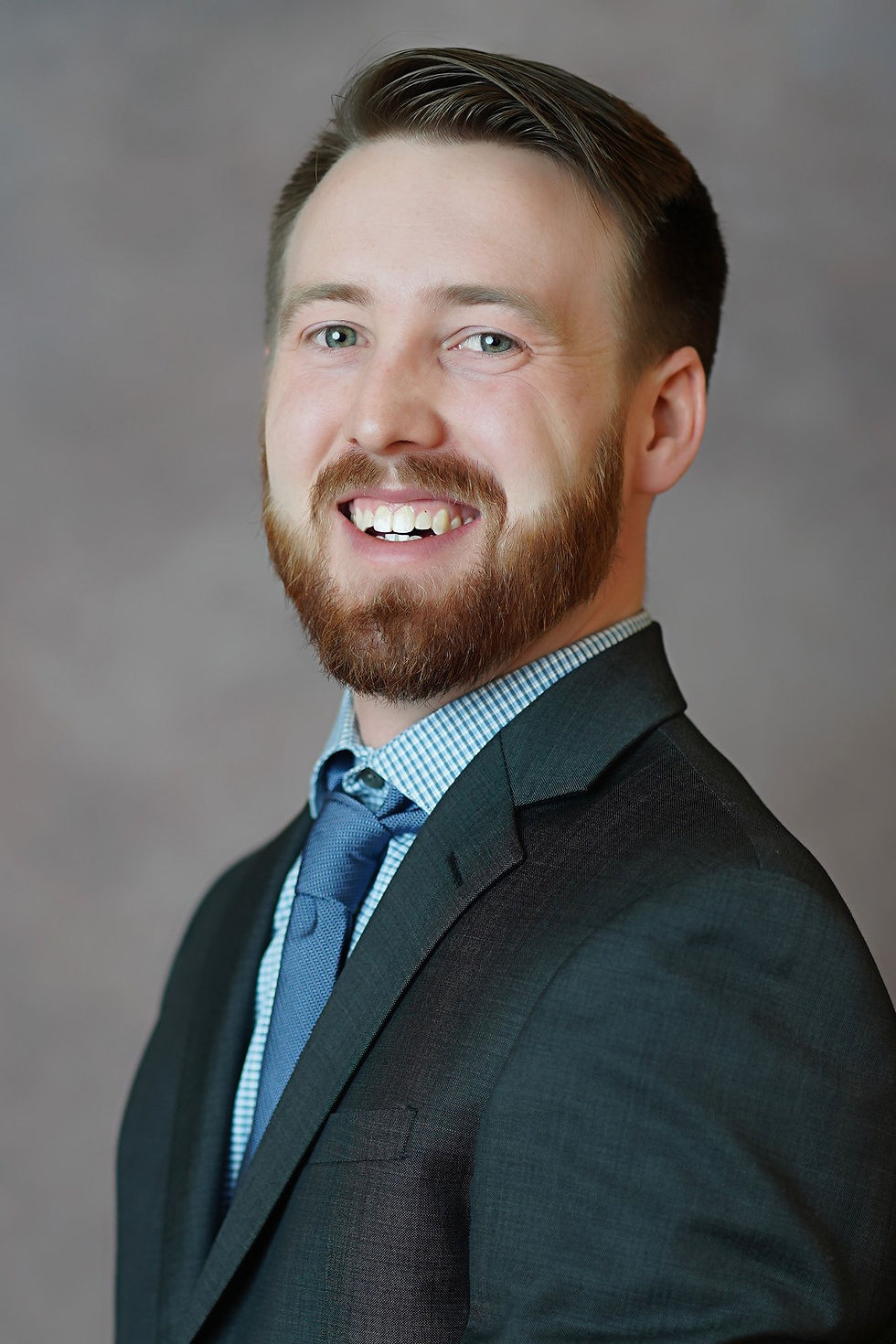 Professional headshot of a man wearing a dark suit with a blue shirt and tie