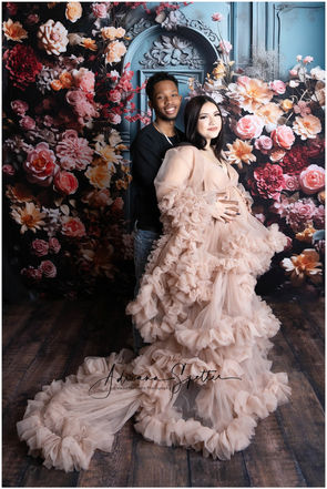 Alamogordo couple posing for a maternity session in front of a backdrop with a blue wall and floral arrangement

