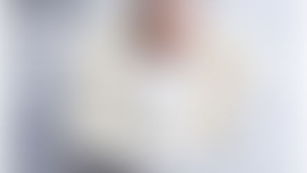 Newborn boy swaddled in soft white wrap, asleep on cream nest during studio newborn session.