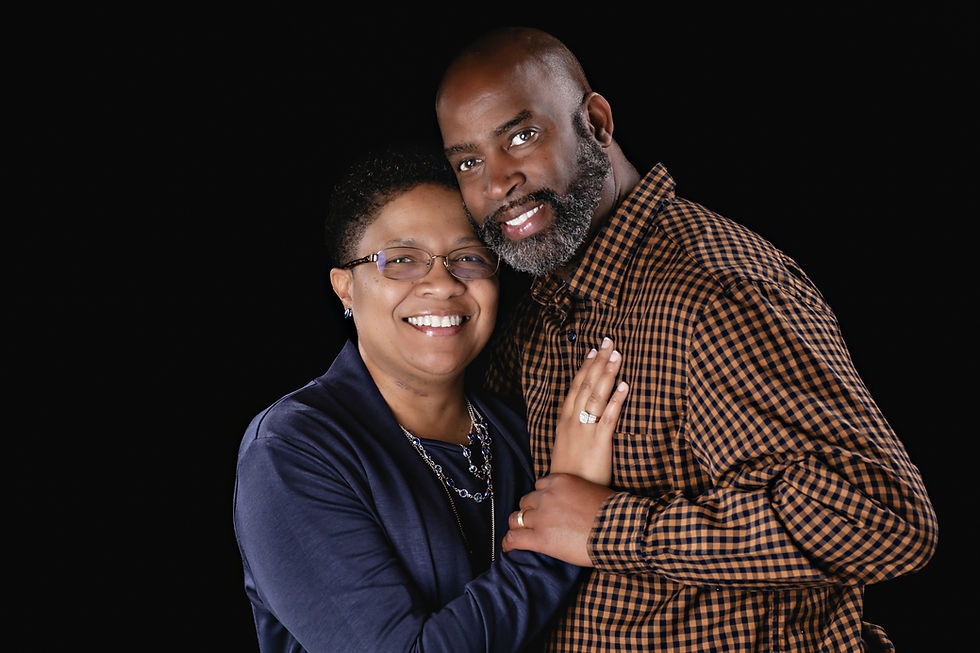 Smiling married couple standing close together against a black background