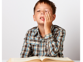 Young boy holds his face in frustration with an open book on the table in front of him