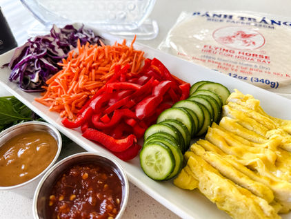 julienned veggies, sliced cucumbers, and eggs on a platter with sauces in foreground
