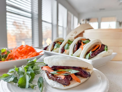 bao buns topped with seared steak, carrots, cilantro, and green onion on serving dishes