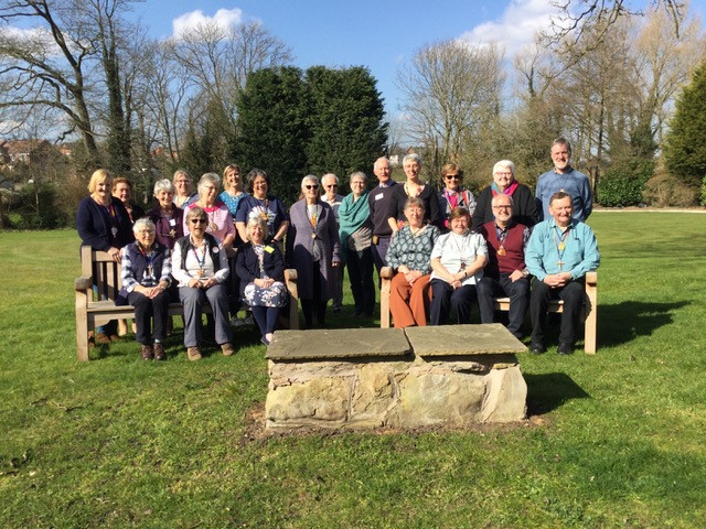 Group of people seated and standing outside on a sunny day