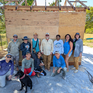 Whatcom WAVES hempcrete shed workshop crew, July 2025, Pacific Northwest. Volunteers and builders pose in front of a timber-framed structure ready for hempcrete infill.