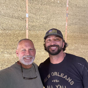 Wade Atteberry and Shawn Ledig smiling in front of a finished hempcrete wall inside the Dash home in Santa Cruz