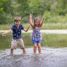 Children laughing and splashing together in the water during a playful family photo session in Austin