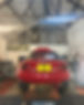 A red car with a black convertible top is raised on a ramp inside a garage with exposed metal beams and automotive tools