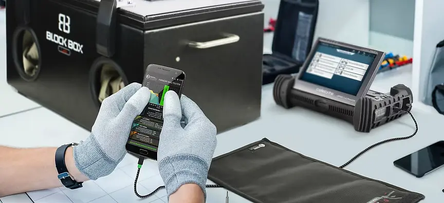 Person using a smartphone, testing equipment, and Faraday bags on a lab bench