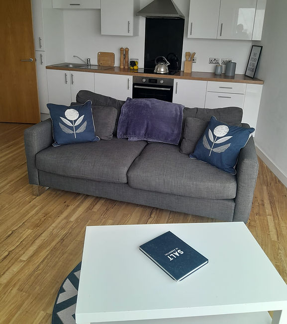 A grey sofa with blue floral pillows and a purple throw blanket