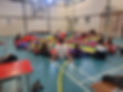 A group of children sits on the floor, holding a colorful parachute
