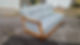 A light blue couch with wooden arms, positioned outdoors on a gravel surface, with a sleeping dog in the background