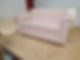 A stylish light pink upholstered loveseat with a piped edge, resting on a wooden surface in a workshop