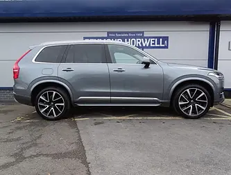 A side view of a gray Volvo SUV parked in front of a dealership