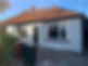 A semi-detached house with a white exterior, black door, large windows, and blue and green trash bins placed in front