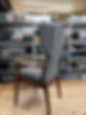 A stylish gray upholstered chair with wooden arms and legs, set against a cluttered workshop backdrop
