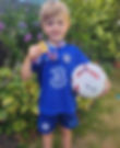 A child in a blue t-shirt holding a medal and ball in a garden