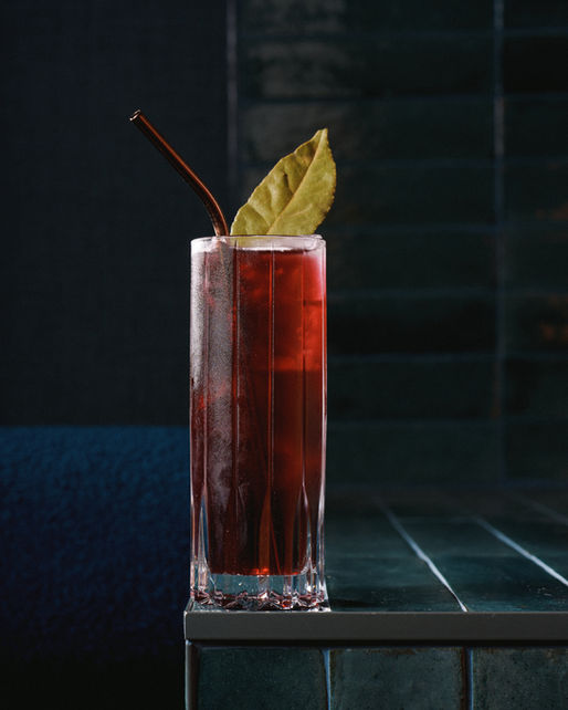 Tall , long red coloured cocktail in a highball with a green leaf on a smart corporate event bar